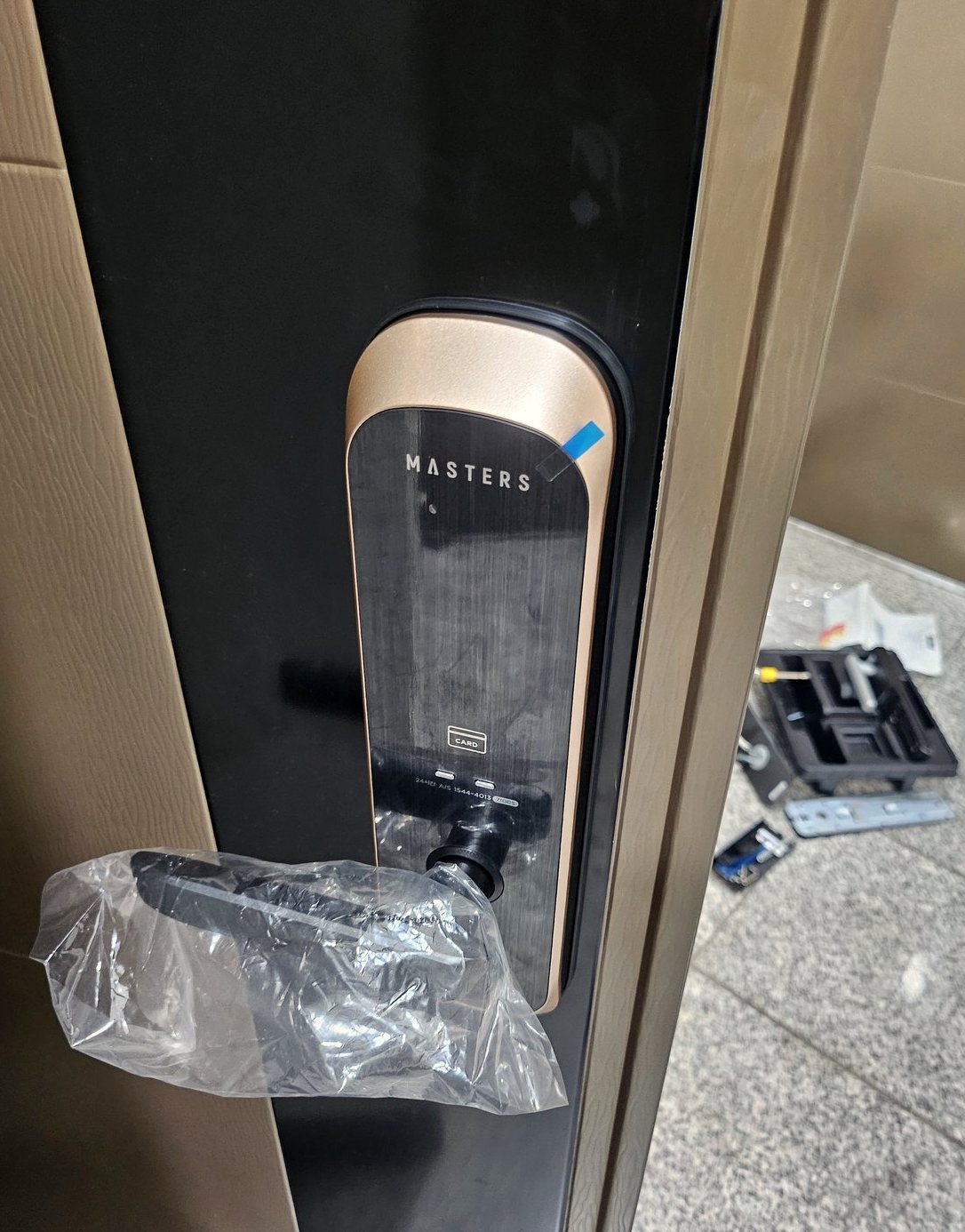 고양시 창릉동 출장 — 검은 문에 단 금색 테 도어락 본체와 비닐 씌운 레버, 오른쪽 바닥의 열린 부품 상자